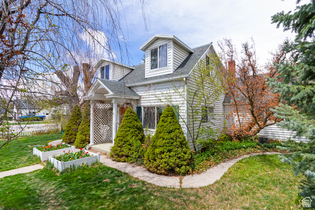 New england style home featuring a shingled roof, a chimney, a garden, and a front yard