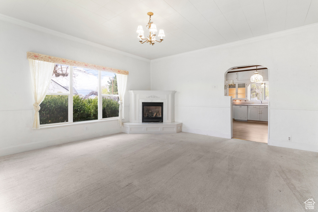 Unfurnished living room featuring crown molding, an inviting chandelier, arched walkways, a glass covered fireplace, and carpet
