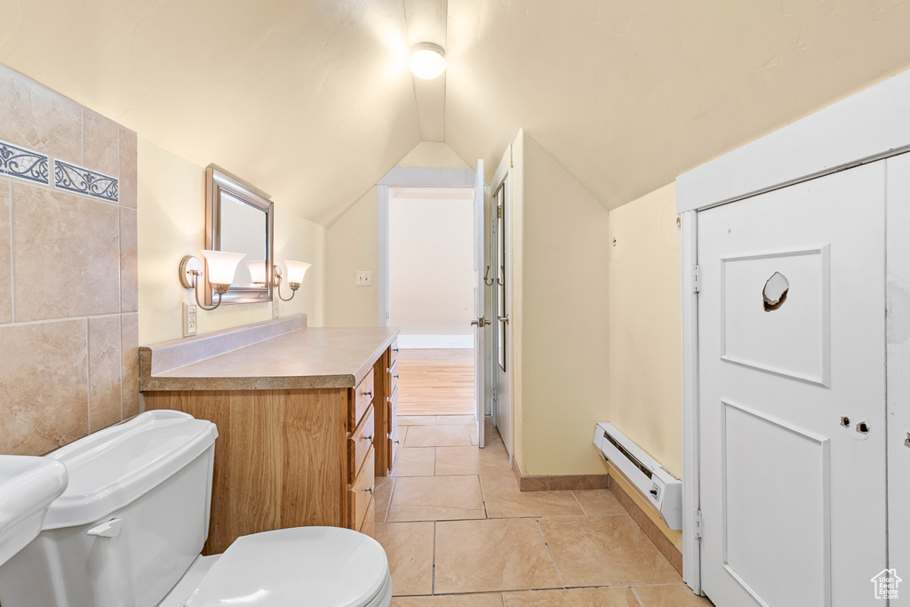 Bathroom with tile patterned flooring, vaulted ceiling, vanity, a baseboard heating unit, and toilet
