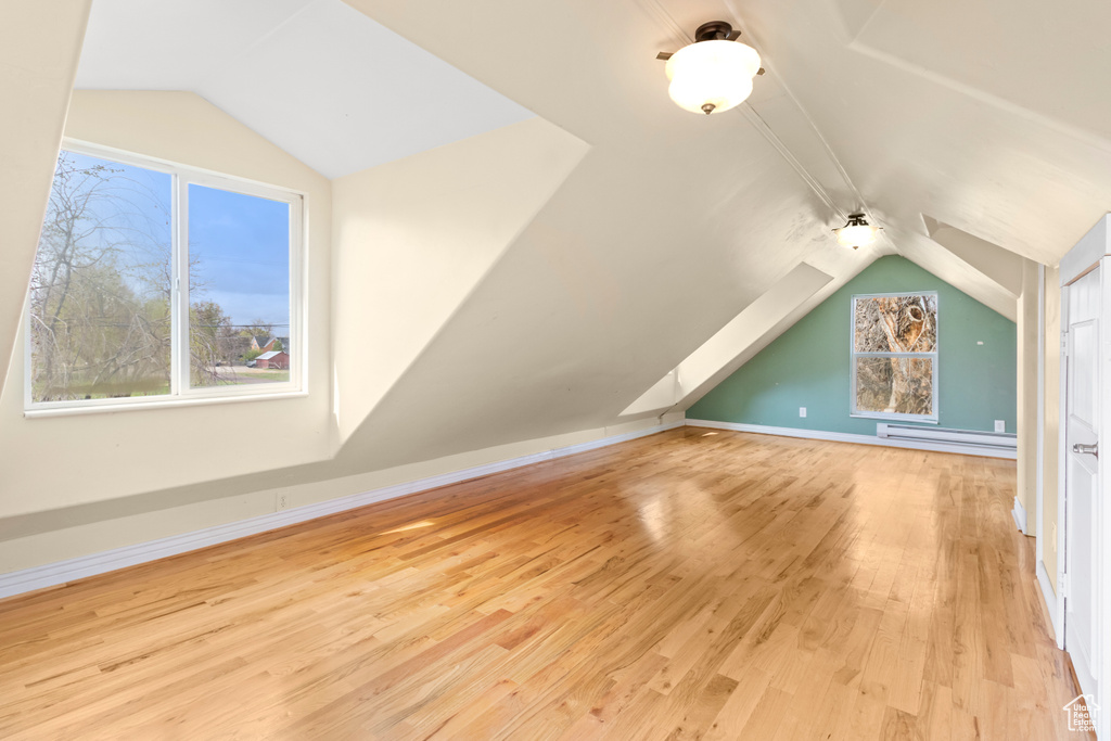 Additional living space featuring vaulted ceiling, baseboards, a baseboard heating unit, and wood finished floors