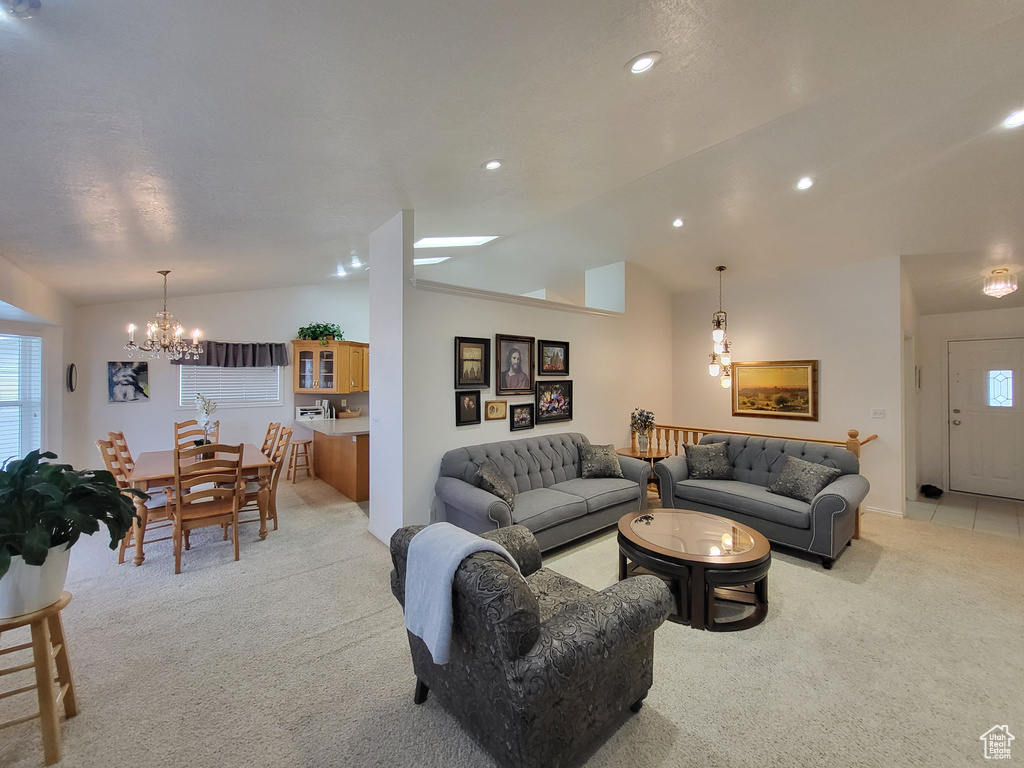 Living area with a chandelier, light colored carpet, a wealth of natural light, and lofted ceiling