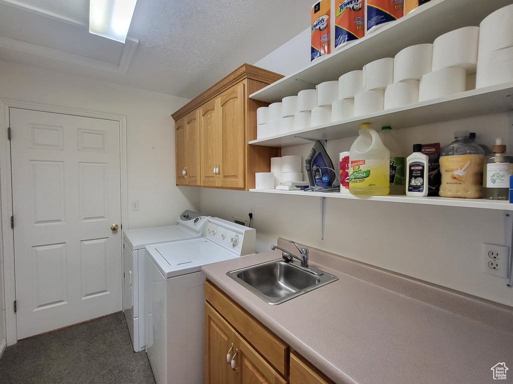 Clothes washing area featuring washing machine and dryer, a textured ceiling, cabinet space, a sink, and carpet