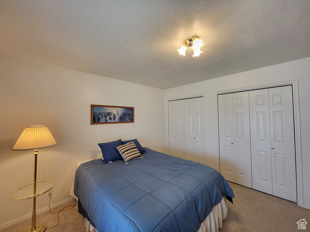 Carpeted bedroom featuring a textured ceiling, multiple closets, and baseboards