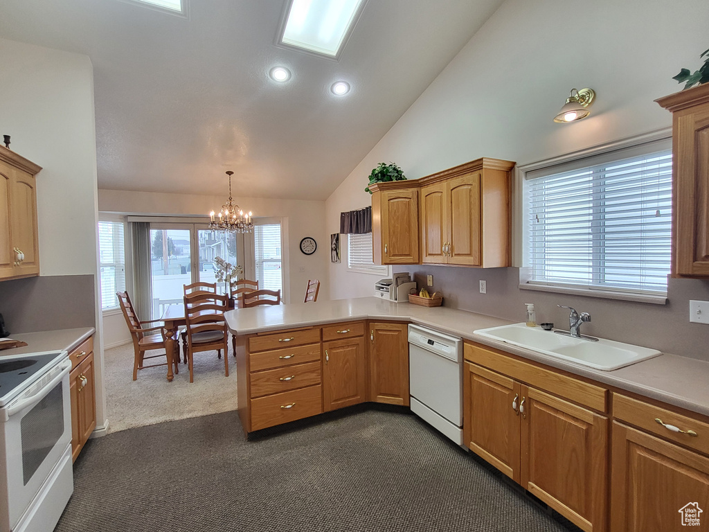 Kitchen featuring a peninsula, white appliances, dark carpet, a sink, and a notable chandelier