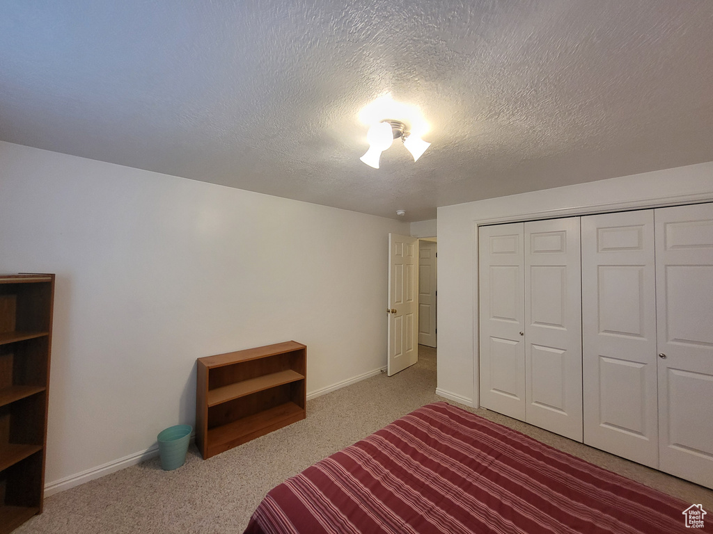 Carpeted bedroom with a closet, a textured ceiling, and baseboards