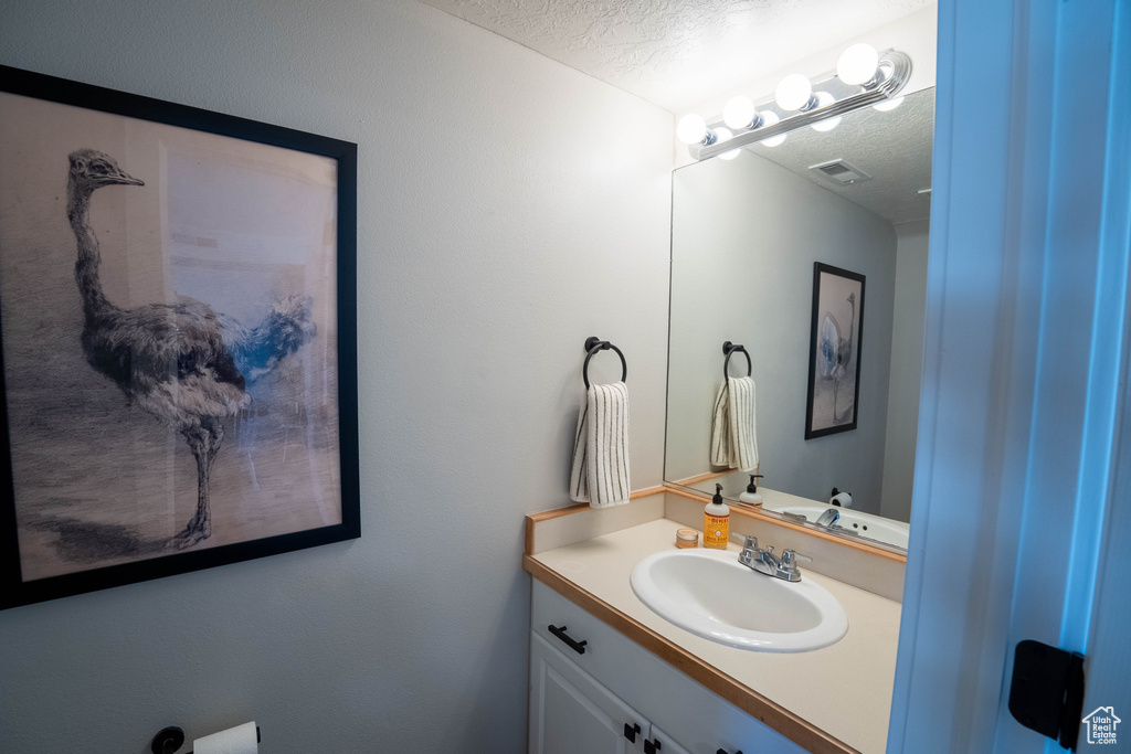 Bathroom with a textured ceiling, visible vents, and vanity