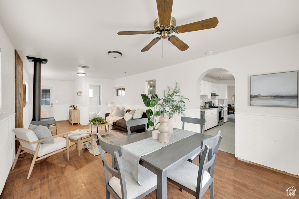 Dining room featuring light wood-style floors, arched walkways, a ceiling fan, and a wood stove