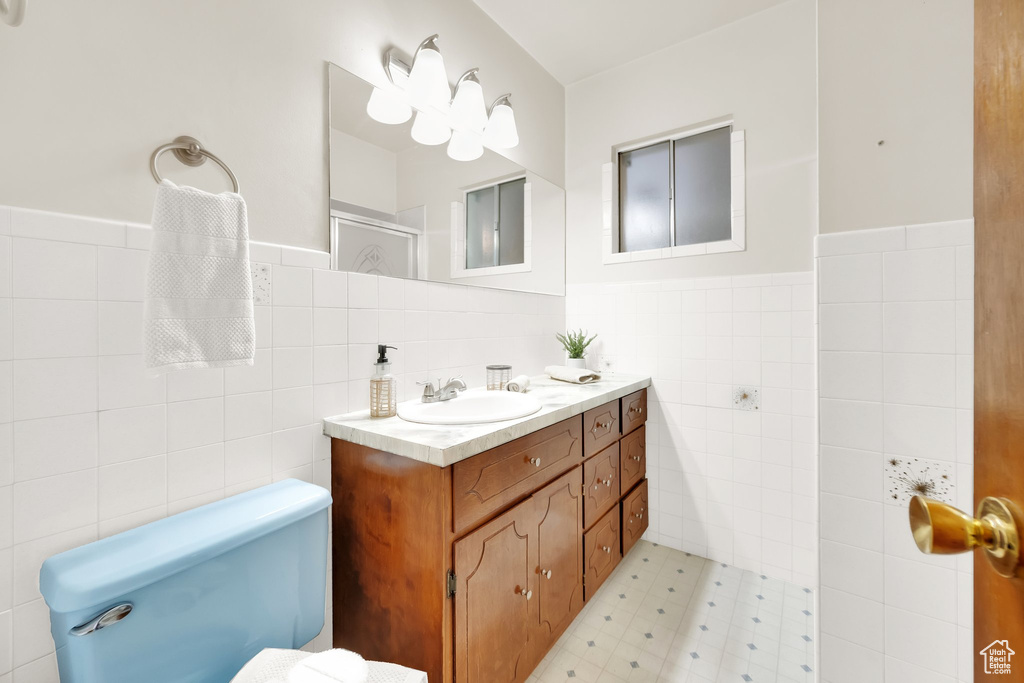 Full bathroom with vanity, toilet, tile walls, and a wainscoted wall