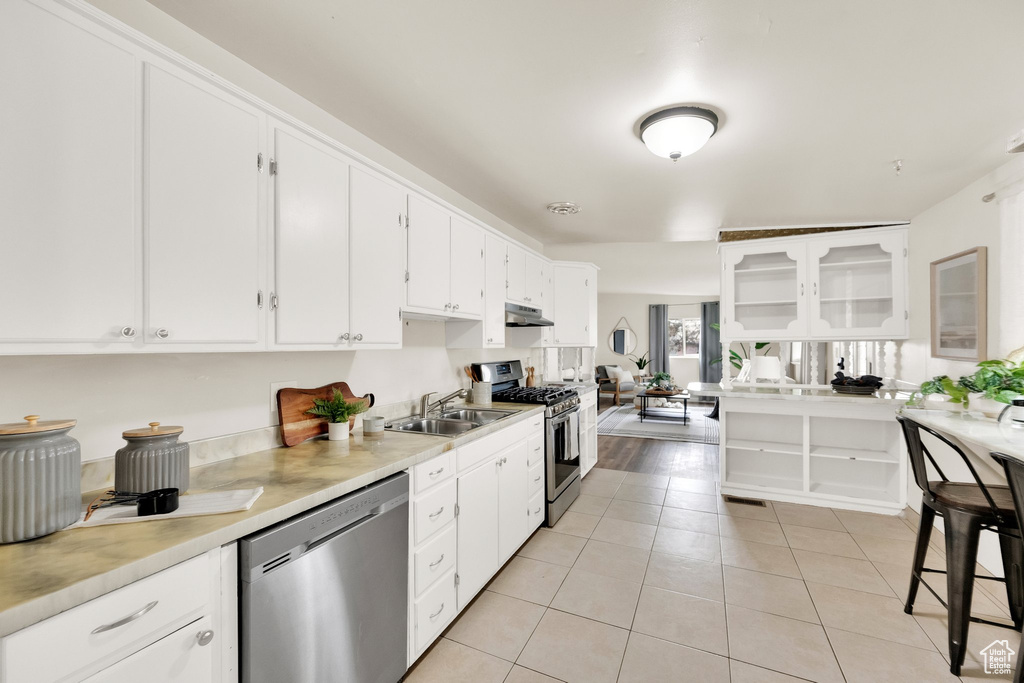Kitchen with white cabinets, a sink, stainless steel appliances, light tile patterned floors, and under cabinet range hood