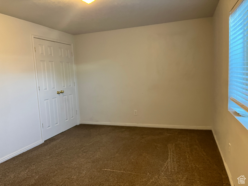 Unfurnished bedroom with baseboards, multiple windows, and dark carpet