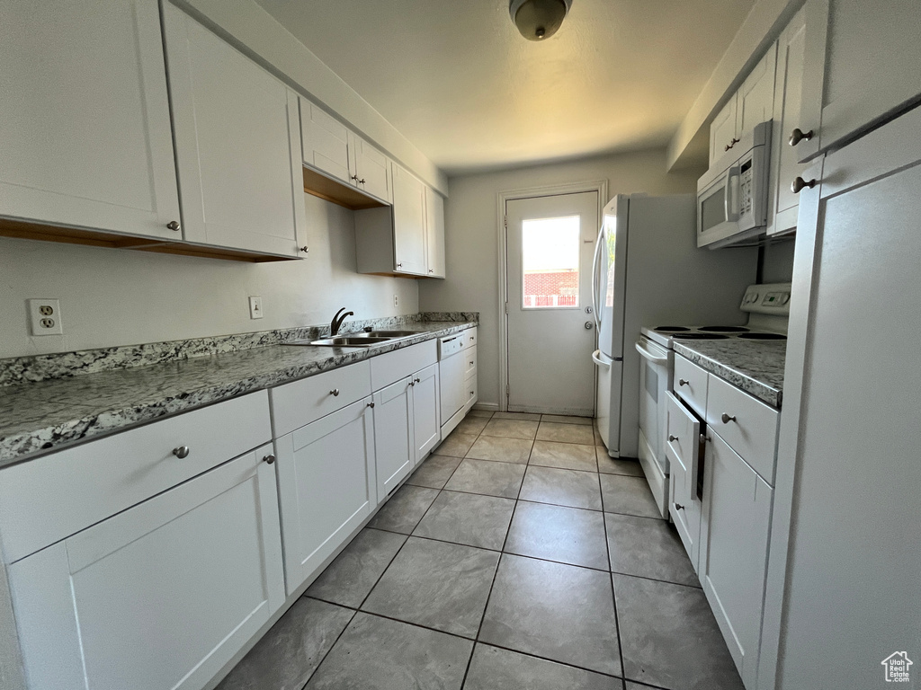 Kitchen featuring a sink, light tile patterned floors, white cabinets, and white appliances
