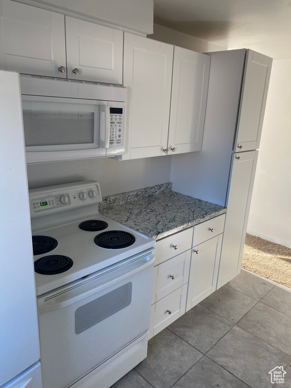 Kitchen with light stone counters, white cabinets, white appliances, and dark tile patterned flooring