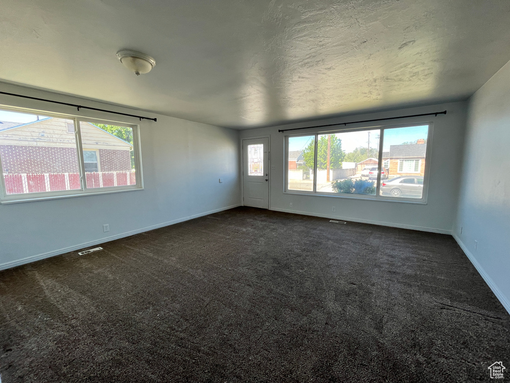 Unfurnished room featuring dark carpet, a wealth of natural light, and visible vents