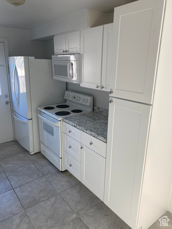Kitchen featuring light stone counters, light tile patterned floors, white cabinets, and white appliances