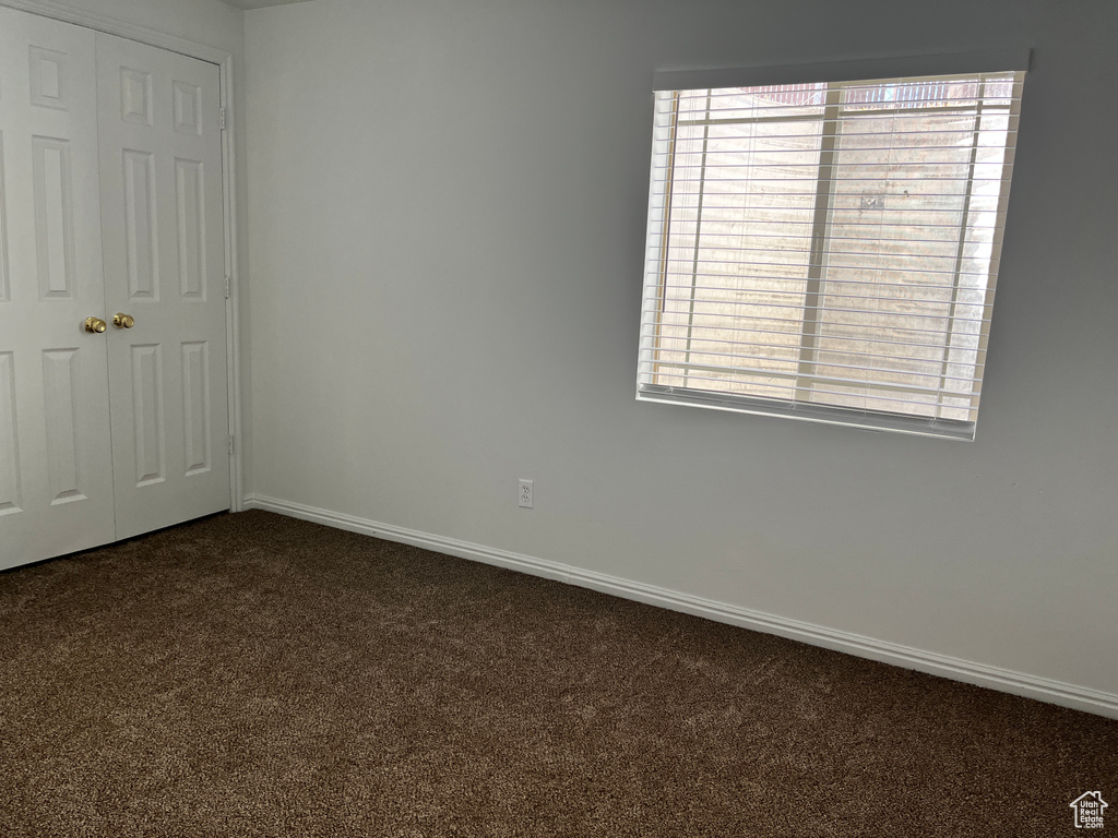 Empty room with baseboards, plenty of natural light, and dark colored carpet