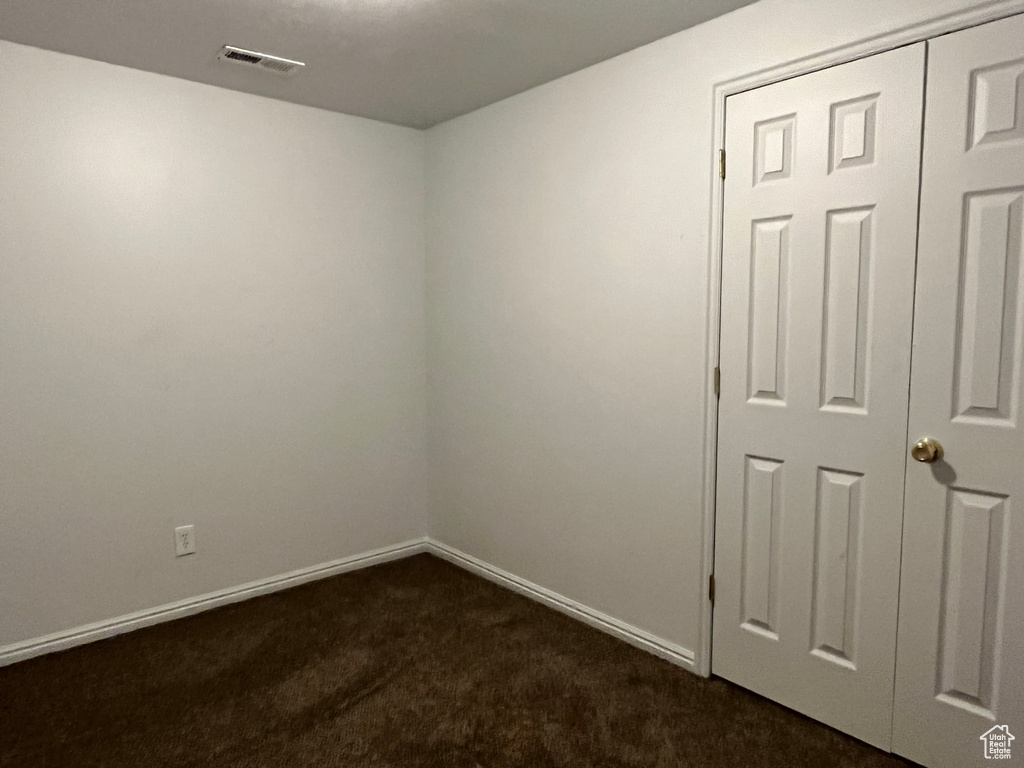 Spare room featuring baseboards, dark colored carpet, and visible vents