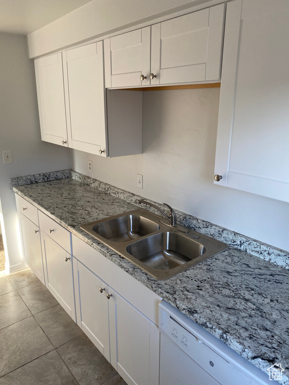 Kitchen with a sink, dishwasher, white cabinets, and dark tile patterned flooring