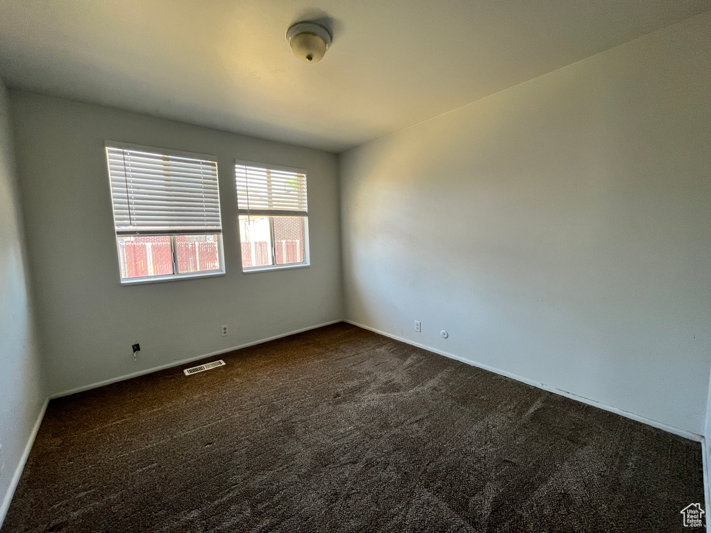 Empty room with baseboards, visible vents, and dark colored carpet