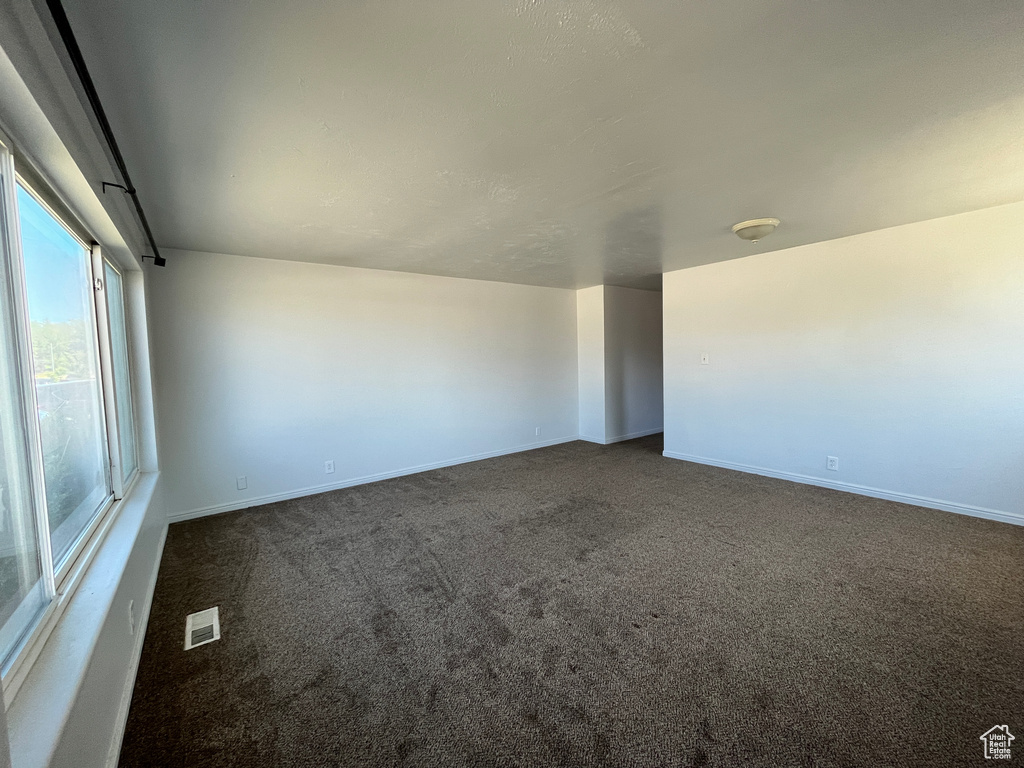 Unfurnished room featuring visible vents, baseboards, and dark colored carpet