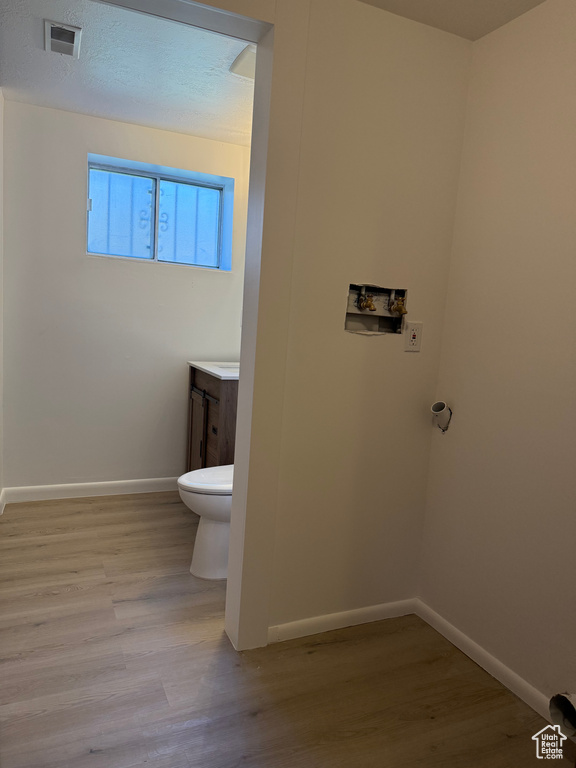 Half bath with visible vents, wood finished floors, vanity, baseboards, and toilet