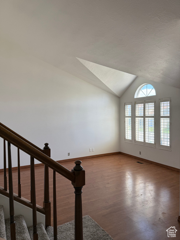 Interior space with stairs, baseboards, wood finished floors, lofted ceiling, and visible vents