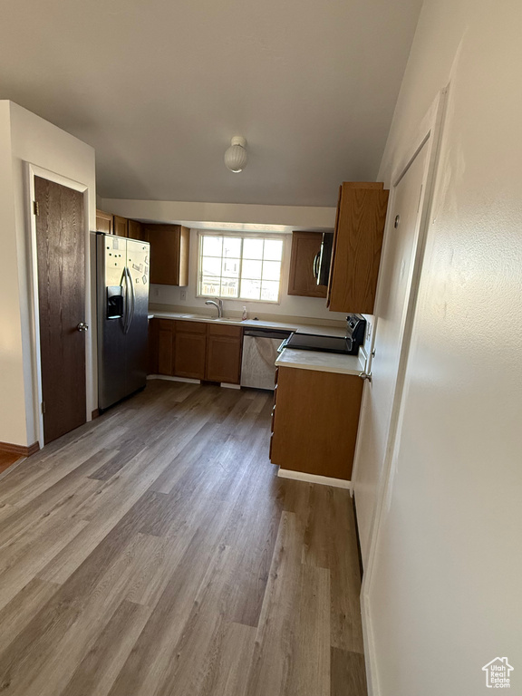 Kitchen with a sink, light countertops, stainless steel appliances, baseboards, and light wood-type flooring