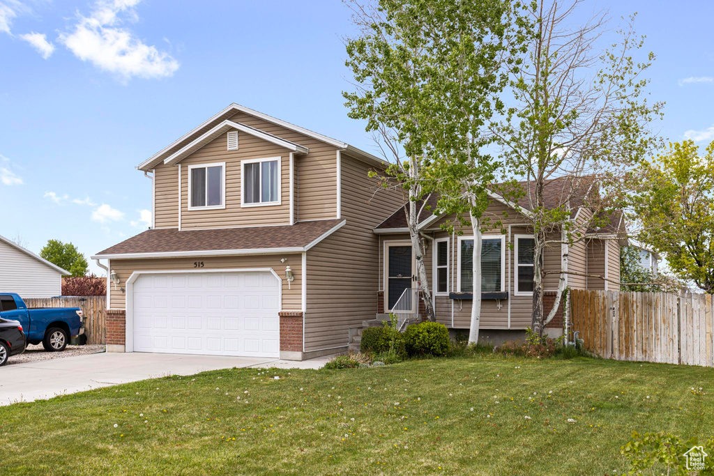Tri-level home with driveway, roof with shingles, fence, a front lawn, and an attached garage