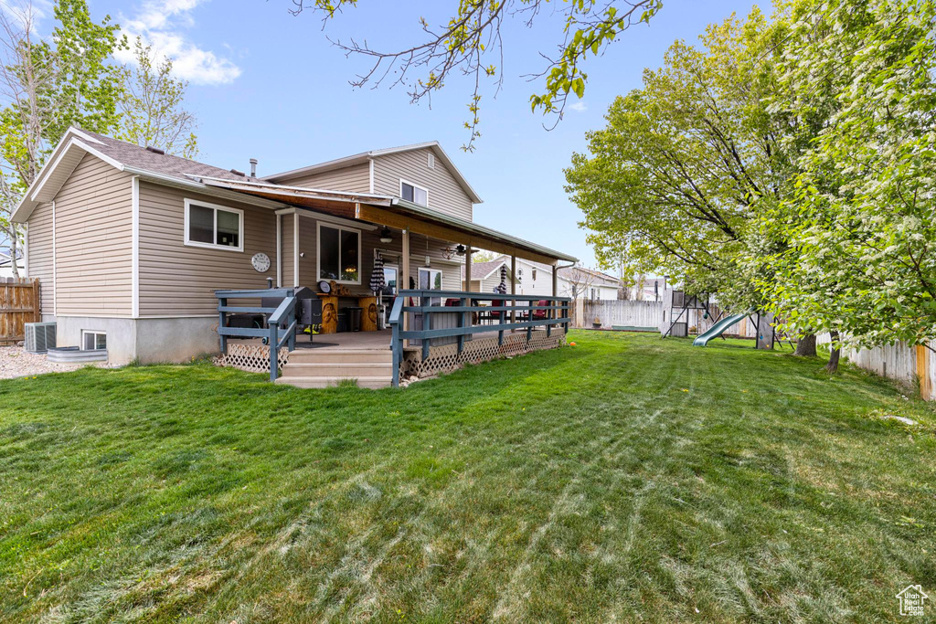 Back of property with a lawn, a fenced backyard, a deck, and cooling unit