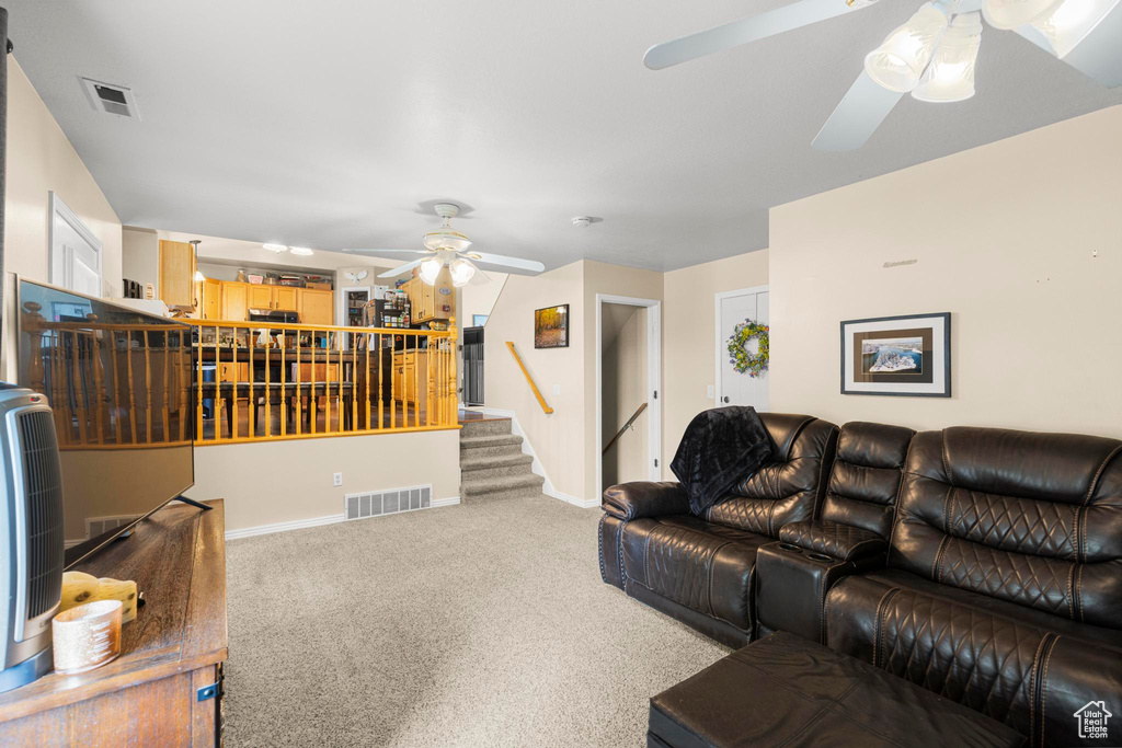 Carpeted living area featuring a ceiling fan, baseboards, visible vents, and stairway