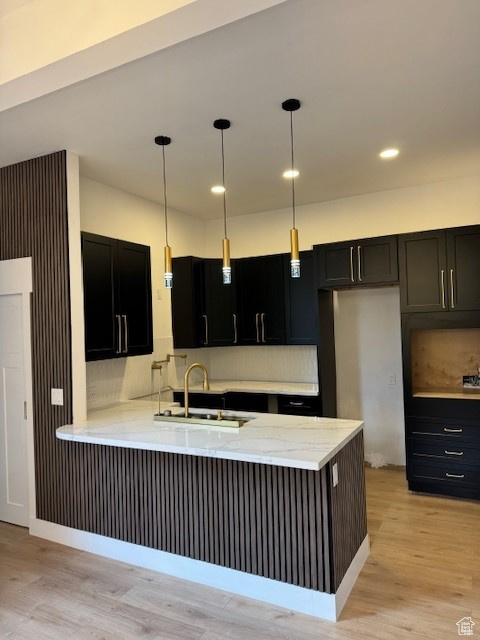 Kitchen featuring dark cabinetry, a sink, light wood-style flooring, and a peninsula