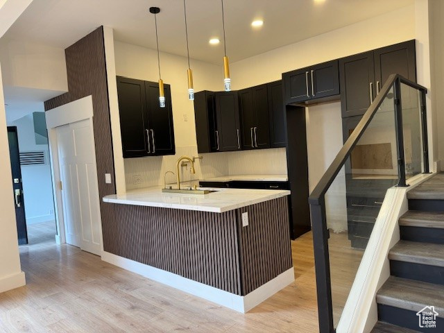 Kitchen featuring a sink, dark cabinetry, a peninsula, light wood-type flooring, and pendant lighting