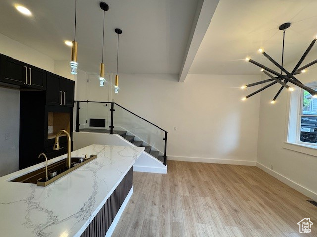 Interior space featuring an inviting chandelier, light stone countertops, light wood-type flooring, dark cabinetry, and decorative light fixtures
