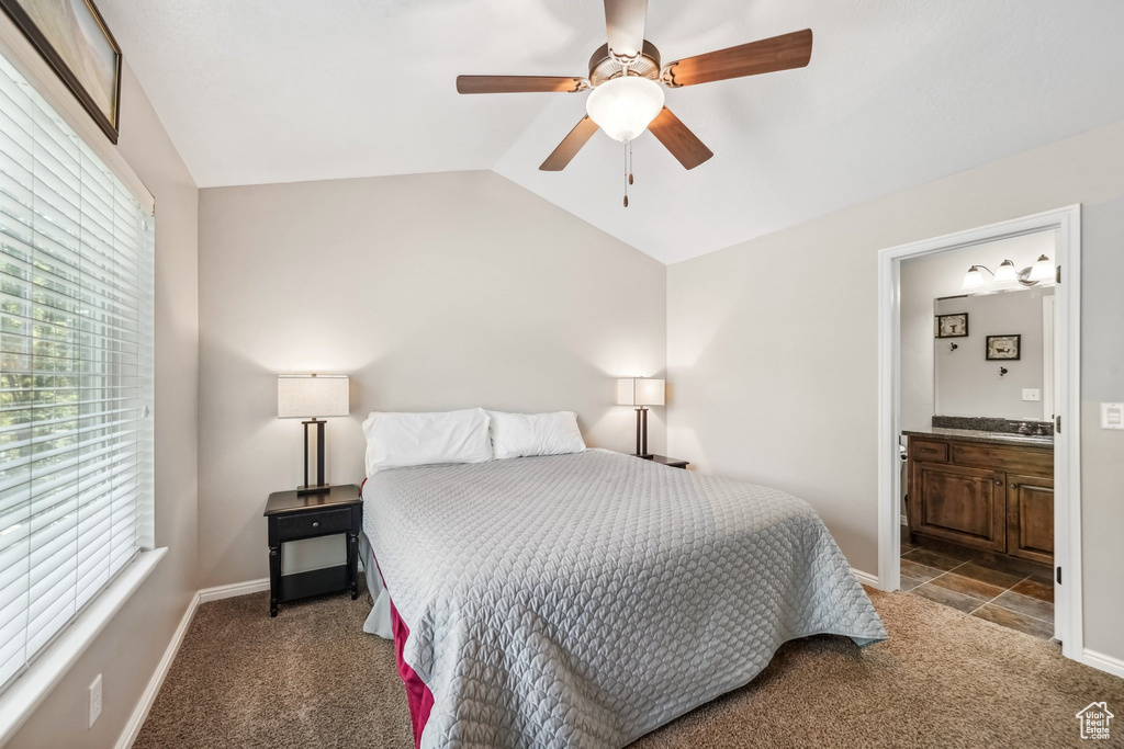 Bedroom featuring carpet flooring, multiple windows, vaulted ceiling, ensuite bathroom, and baseboards