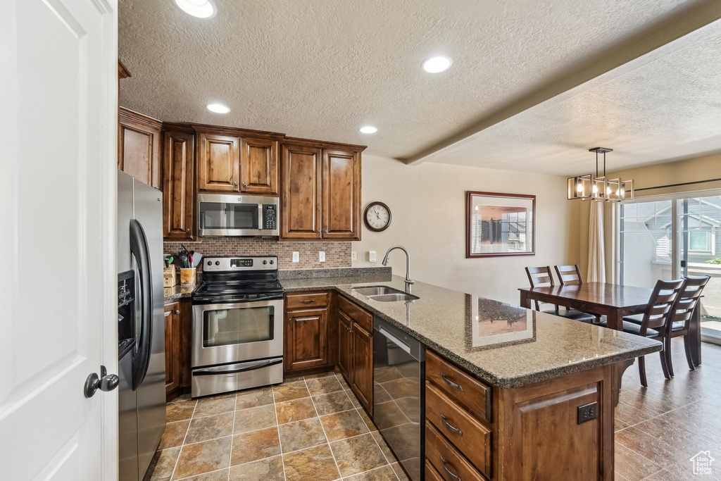 Kitchen featuring appliances with stainless steel finishes, a sink, a peninsula, a textured ceiling, and backsplash