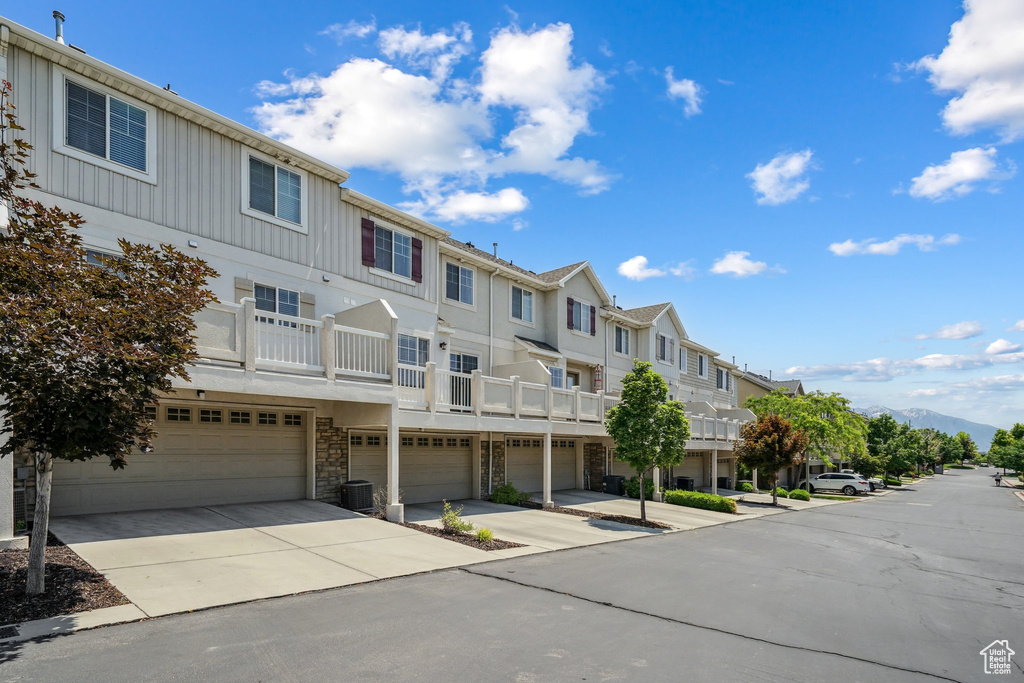 View of property with a residential view, an attached garage, concrete driveway, and central AC