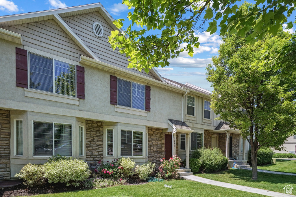 View of front of house featuring stucco siding, stone siding, and a front yard