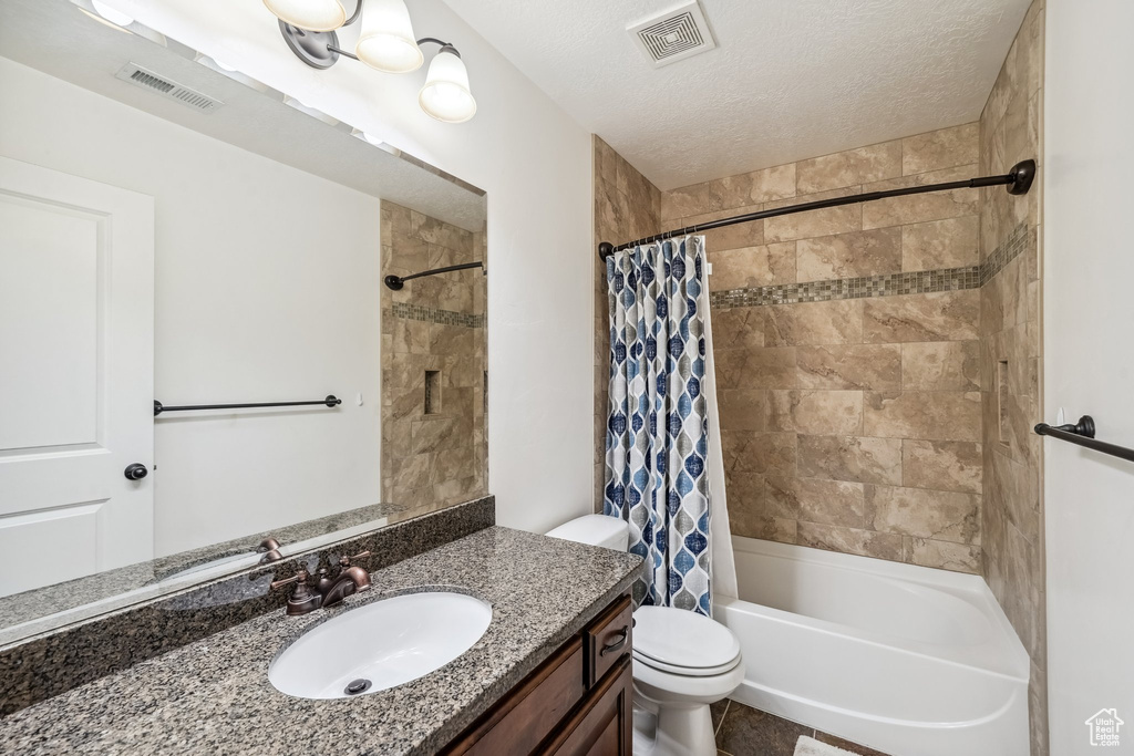 Bathroom featuring vanity, toilet, shower / tub combo, and a textured ceiling