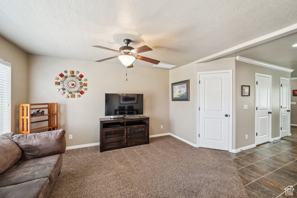 Living room featuring a ceiling fan, a textured ceiling, baseboards, and ornamental molding