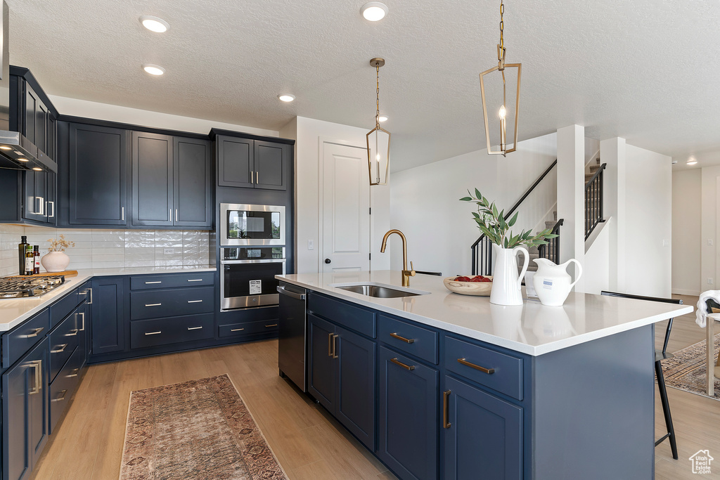 Kitchen with appliances with stainless steel finishes, a breakfast bar, a sink, light wood-style flooring, and tasteful backsplash