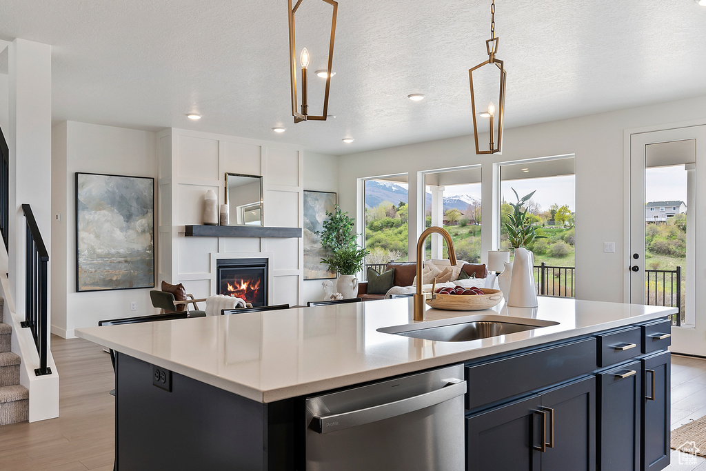 Kitchen with stainless steel dishwasher, a sink, light wood-style flooring, and an island with sink