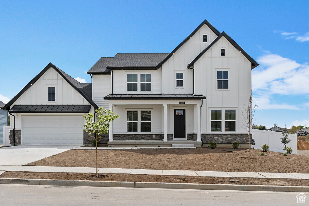 Modern farmhouse with a porch, board and batten siding, a standing seam roof, fence, and concrete driveway