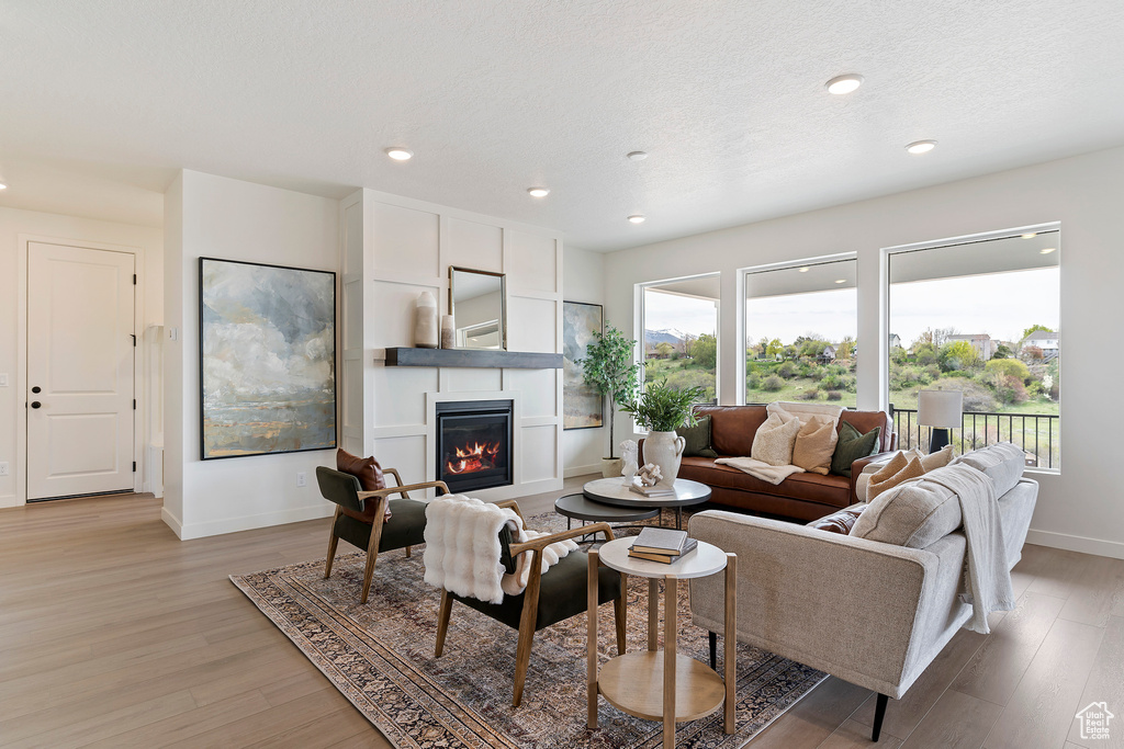 Living area with a glass covered fireplace, baseboards, recessed lighting, and light wood-type flooring