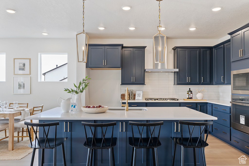 Kitchen with appliances with stainless steel finishes, a sink, a breakfast bar area, light countertops, and wall chimney exhaust hood