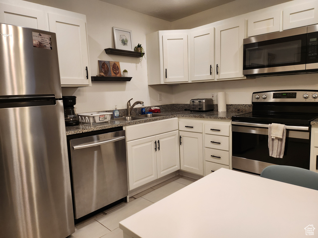 Kitchen with open shelves, white cabinets, a sink, light tile patterned floors, and stainless steel appliances