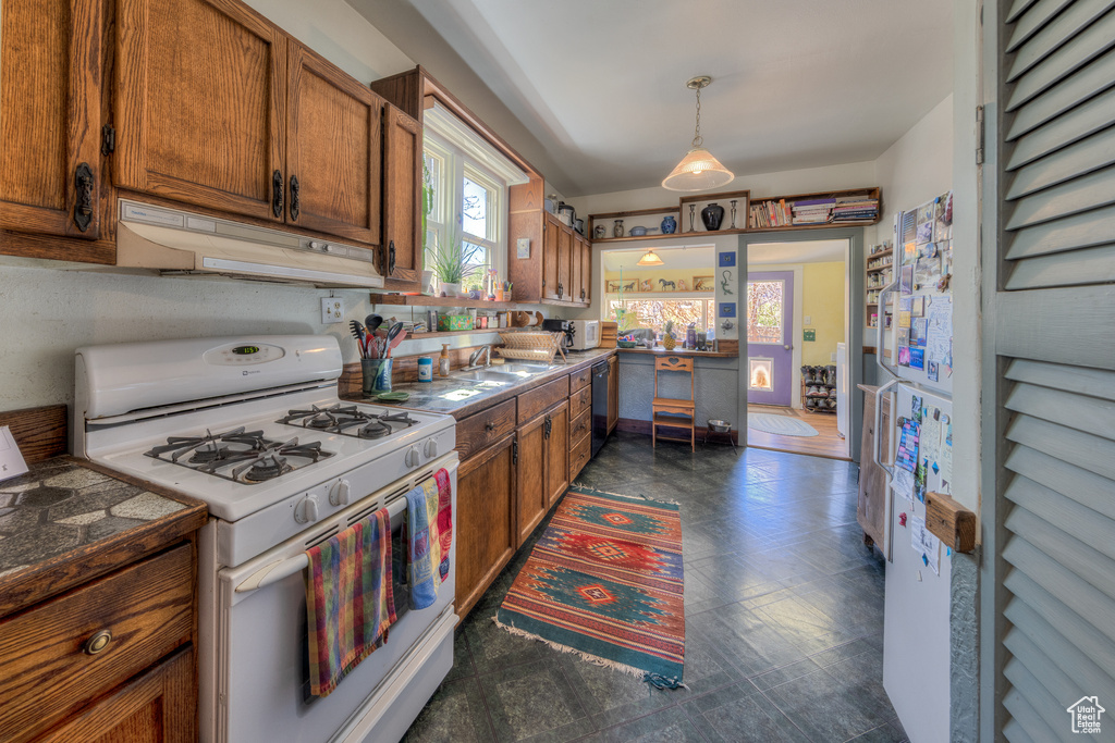 Kitchen featuring white gas range oven, under cabinet range hood, brown cabinetry, and dishwasher