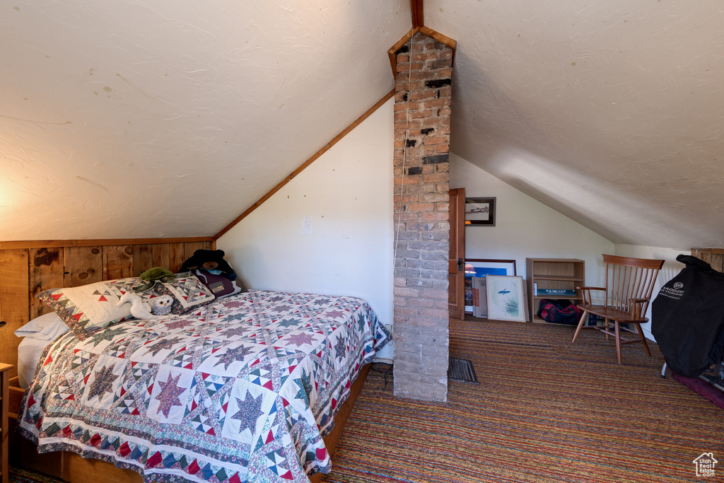 Carpeted bedroom with a textured ceiling, lofted ceiling, and wood walls