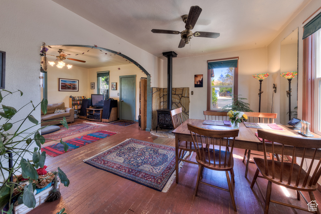 Dining space with a ceiling fan, a wood stove, wood-type flooring, and arched walkways