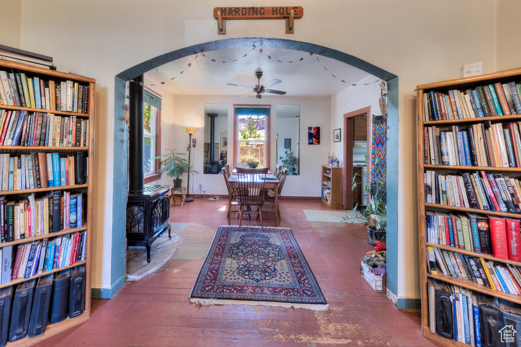 Living area with a wood stove, ceiling fan, arched walkways, and wood-type flooring
