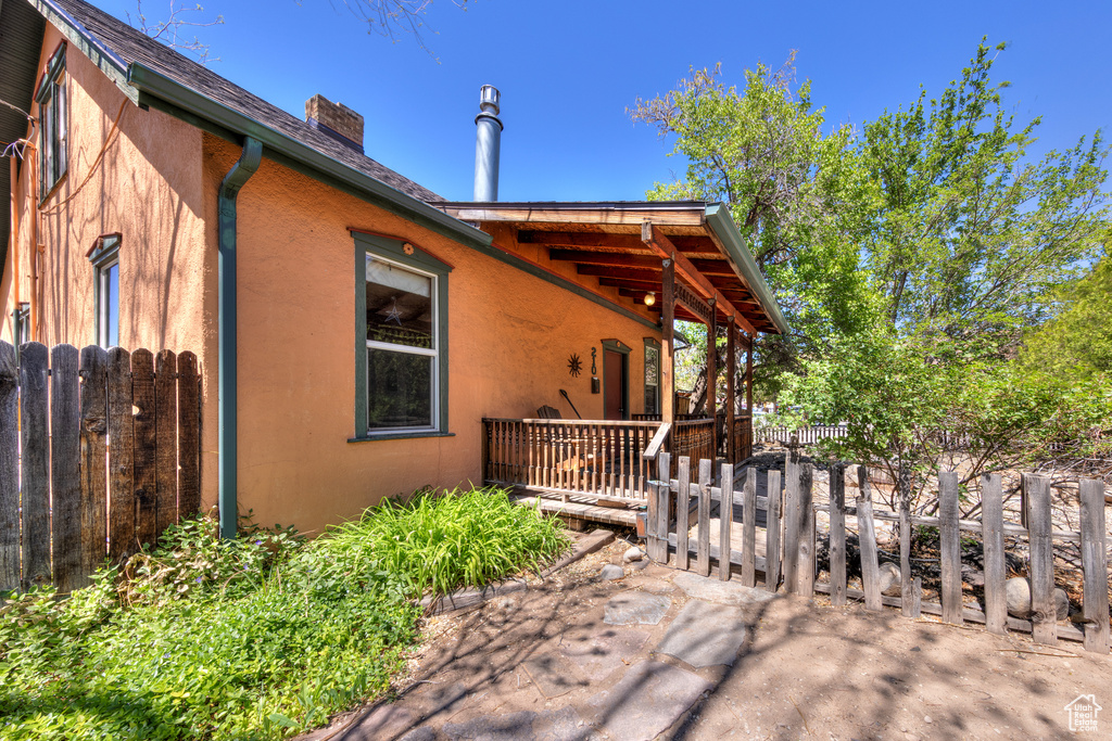 View of side of home featuring a chimney, fence, stucco siding, and a deck