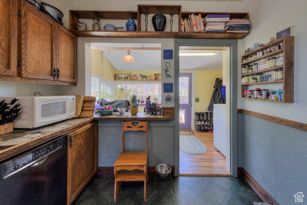 Kitchen featuring dishwasher, white microwave, tile countertops, and brown cabinets
